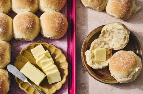 Big-Batch Quick Dinner Rolls on a baking sheet and two on a plate with butter. - select to zoom