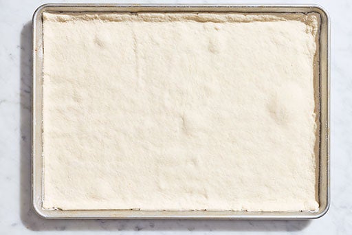 Raw gluten-free pizza dough on a rectangular sheet pan.