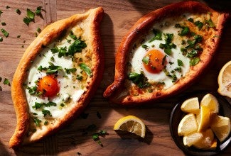 Two freshly baked Khachapuri (Georgian Cheese Breads) topped with soft-baked eggs and fresh herbs