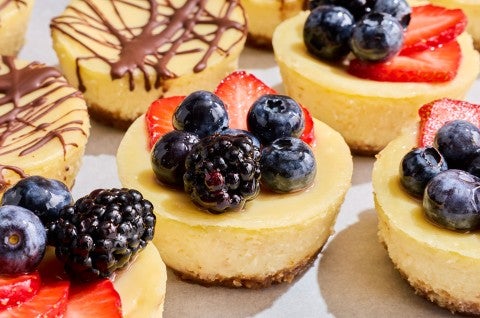The side of golden yellow Mini Cheesecakes topped with fresh berries and others with chocolate drizzle. - select to zoom