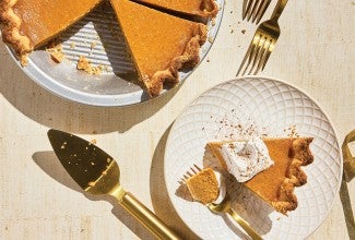 A slice of Smooth and Spicy Pumpkin Pie on a plate with the full pie in the background