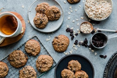 An overhead photo of oatmeal raisin cookies, some rest on a cooling rack while others are shingled together on small plates. The cookies have craggly tops from the oats with puffy centers and golden edges. 