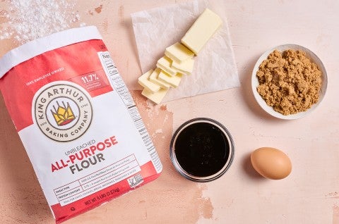 Ingredients to make Soft Brown Sugar Cookies laid out on a warm countertop showing butter, brown sugar, an egg, vanilla, and all-purpose flour. - select to zoom