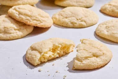Sourdough Sugar Cookies laid out on a counter showing one of the cookies split in half with a slightly cakey interior and crumbs.